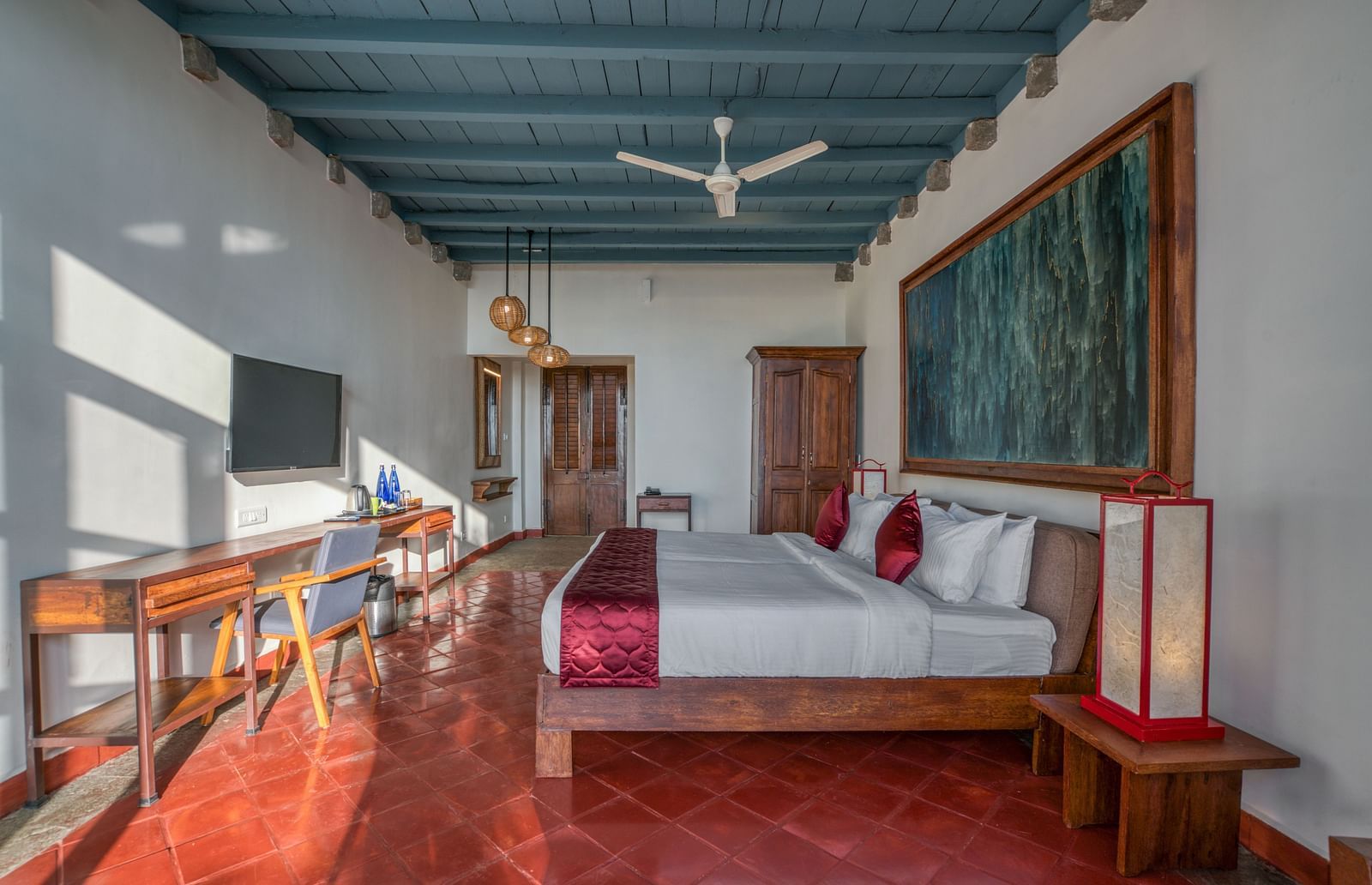 Bedroom with a king-size bed, colorful artwork, wooden furniture, and a ceiling fan, featuring a mix of modern and traditional decor. | Mango Hill, Yercaud