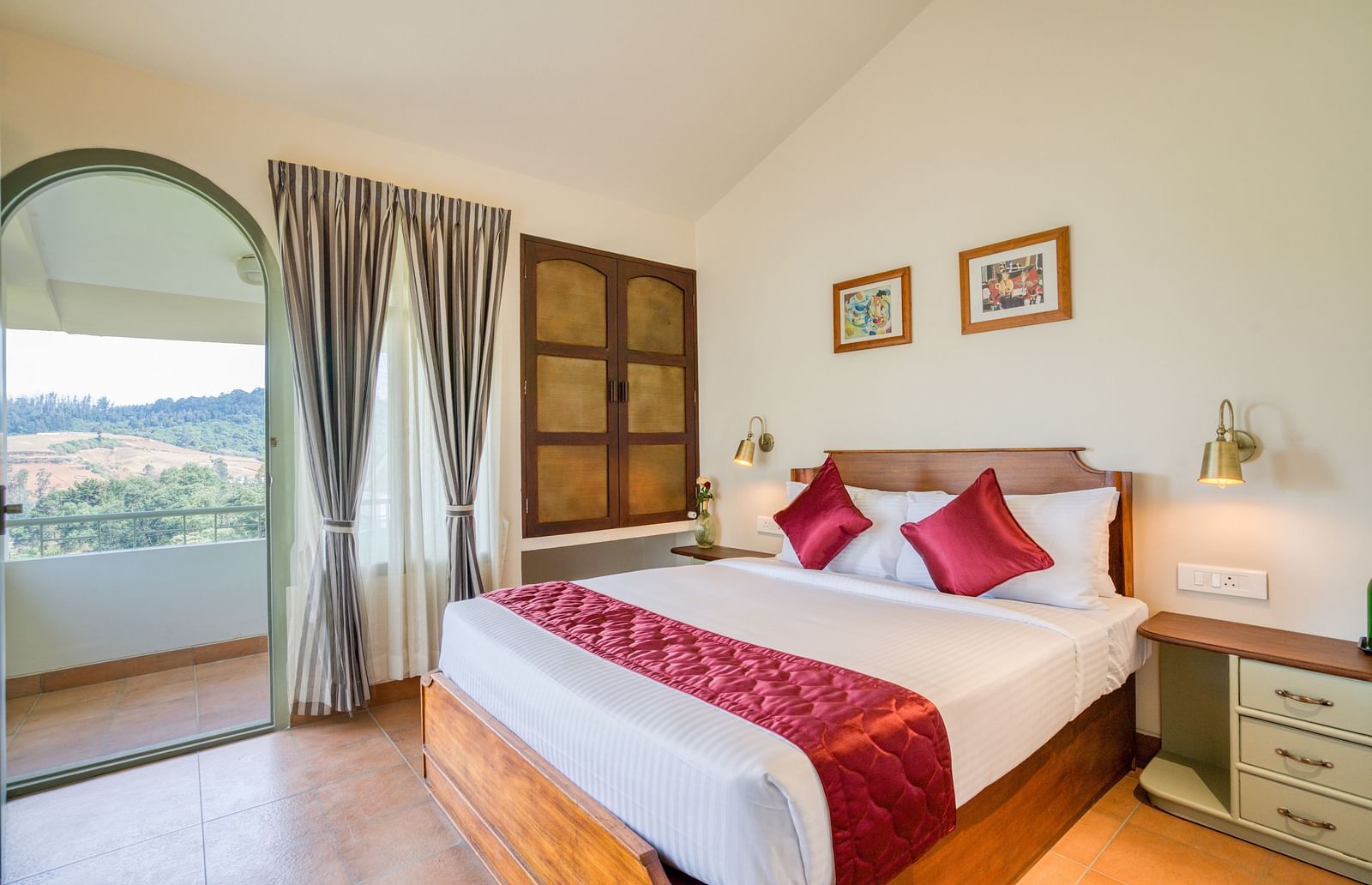 A double bed with red pillows and runner inside bedroom villa with a balcony | Mango Hill Shola Ooty