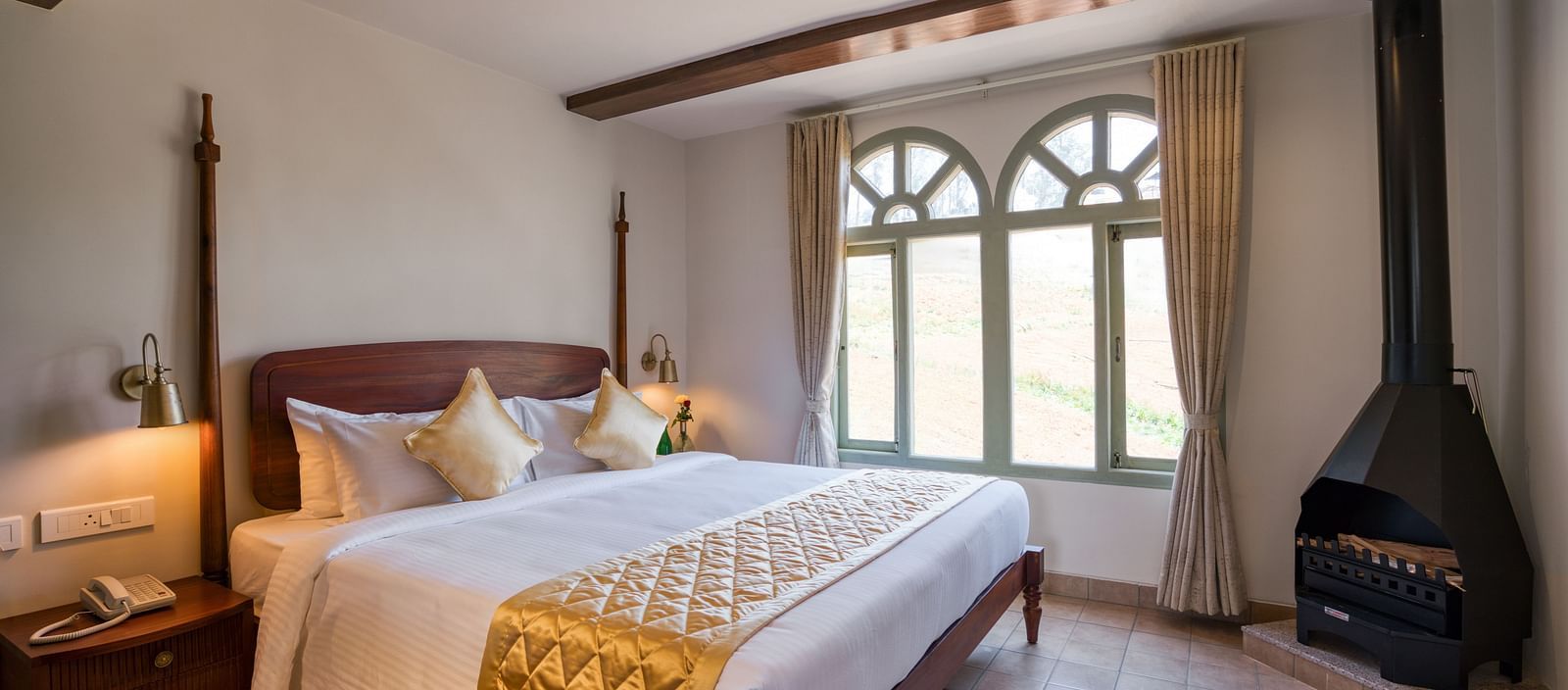 A double bed with a fireplace in the corner inside junior suite | Mango Hill Shola Ooty