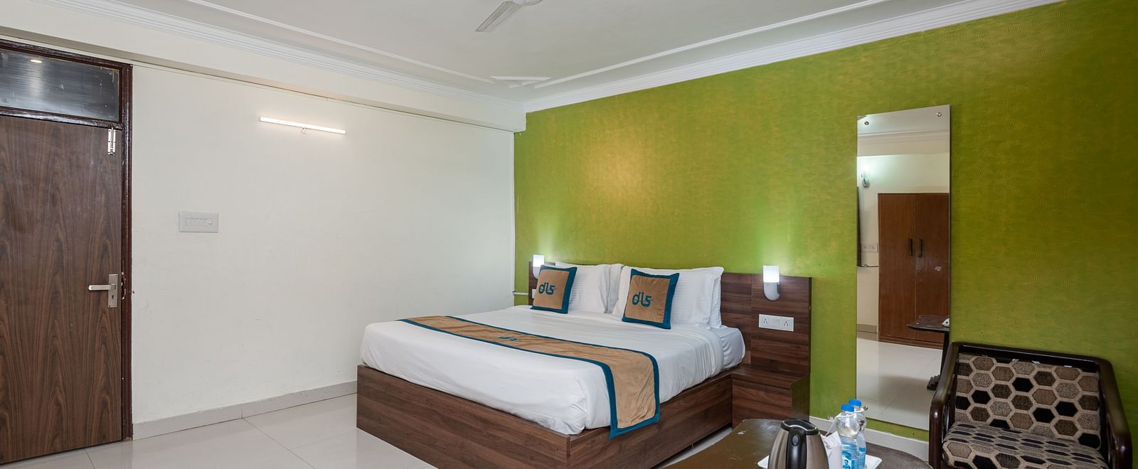 Image of a room with a green wall, king size bed, a seating area with round table and two chairs | DLS Anupam Resort, Dharamshala