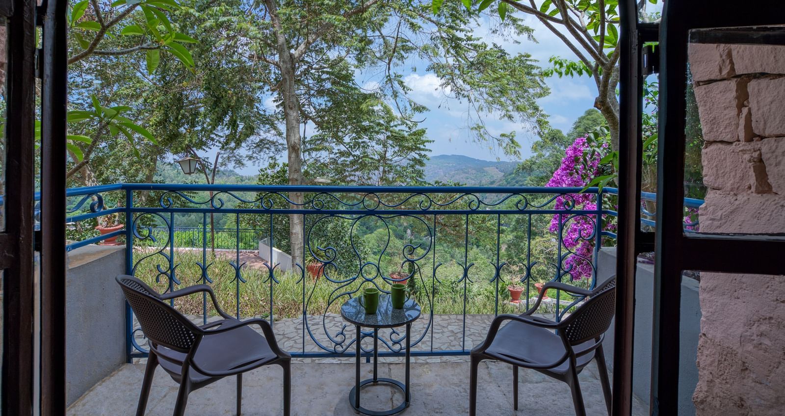 Balcony with two chairs and a table, overlooking a lush green landscape and vibrant flowers. | Mango Hill, Yercaud