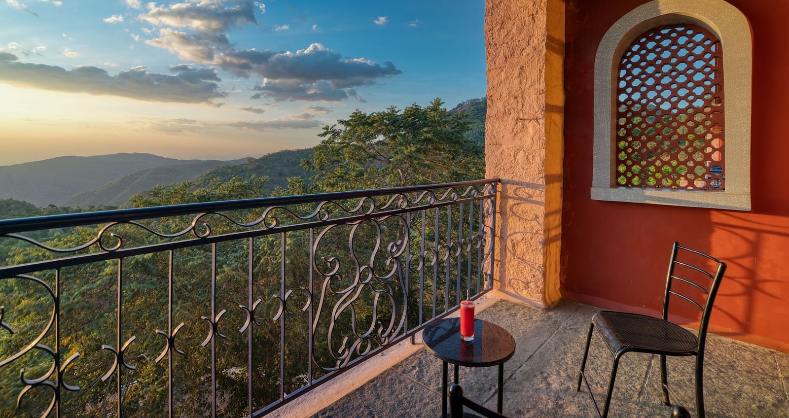 Balcony with two chairs and a table overlooking a lush green valley and distant mountains during sunset.  | Mango Hill, Yercaud