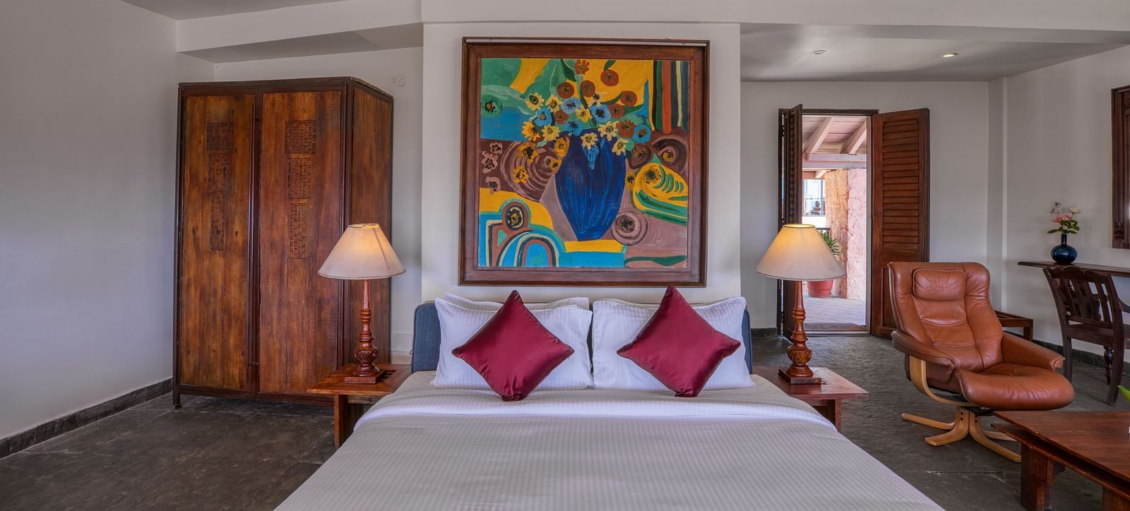Hotel room featuring a comfortable bed with red accents, wooden furniture, and vibrant artwork. | Mango Hill, Yercaud