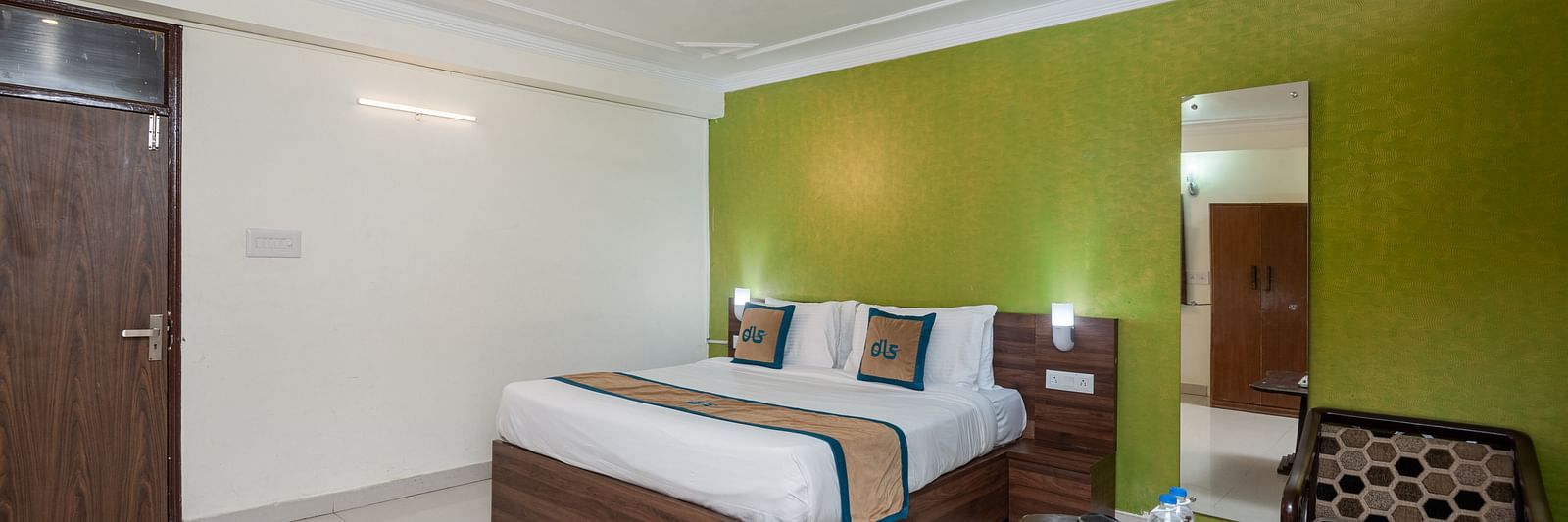 Image of a room with a green wall, king size bed, a seating area with round table and two chairs | DLS Anupam Resort, Dharamshala