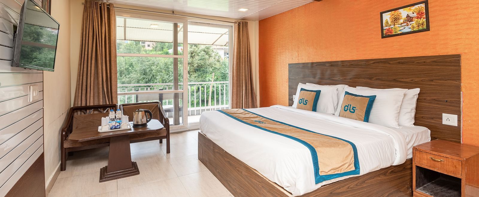 Image of a king size bed in a room with orange coloured wall and couch placed in one corner with a balcony | DLS Anupam Resort, Dharamshala