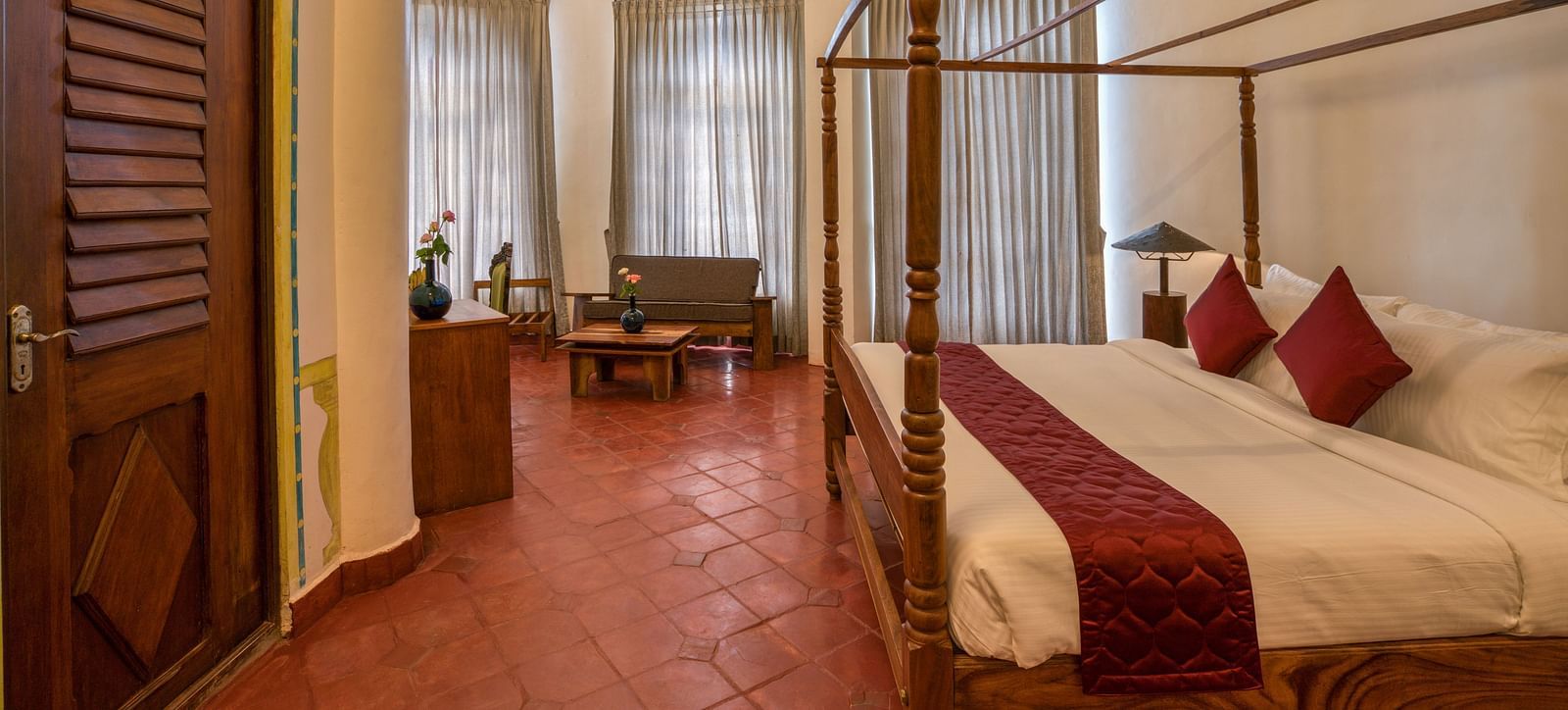 A room with four-poster bed, large windows covered by curtains and as a sitting area at one corner of the room | Mango Hill, Yercaud