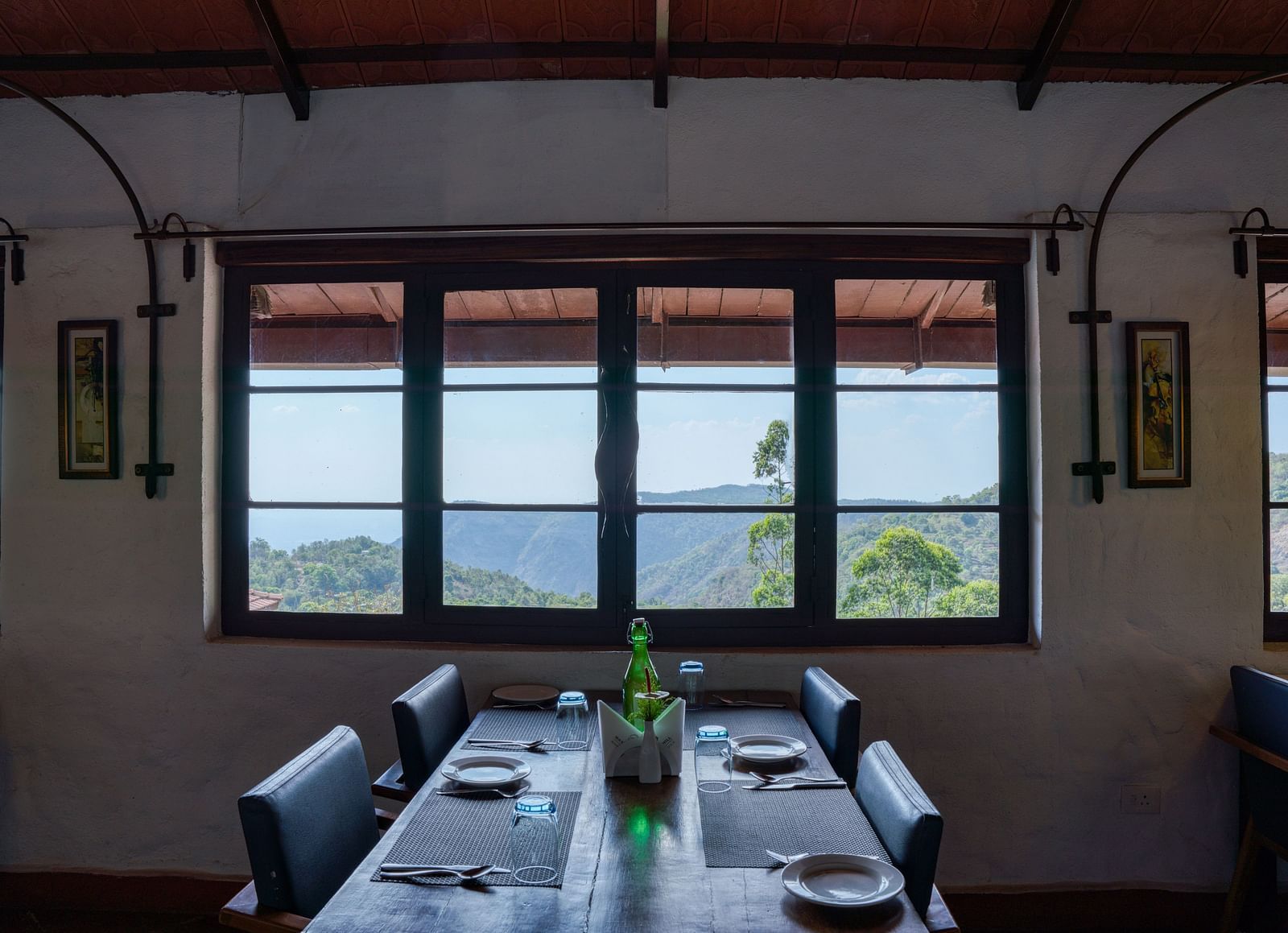 Dining table set near large windows with a scenic view of the hills and greenery. | Mango Hill, Yercaud