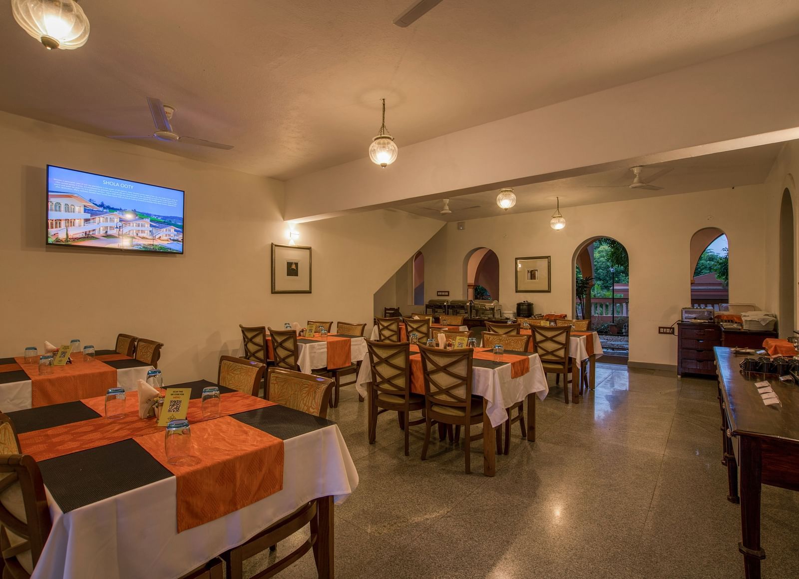 Dinning space with chairs and tables and a TV hanging on the wall.
