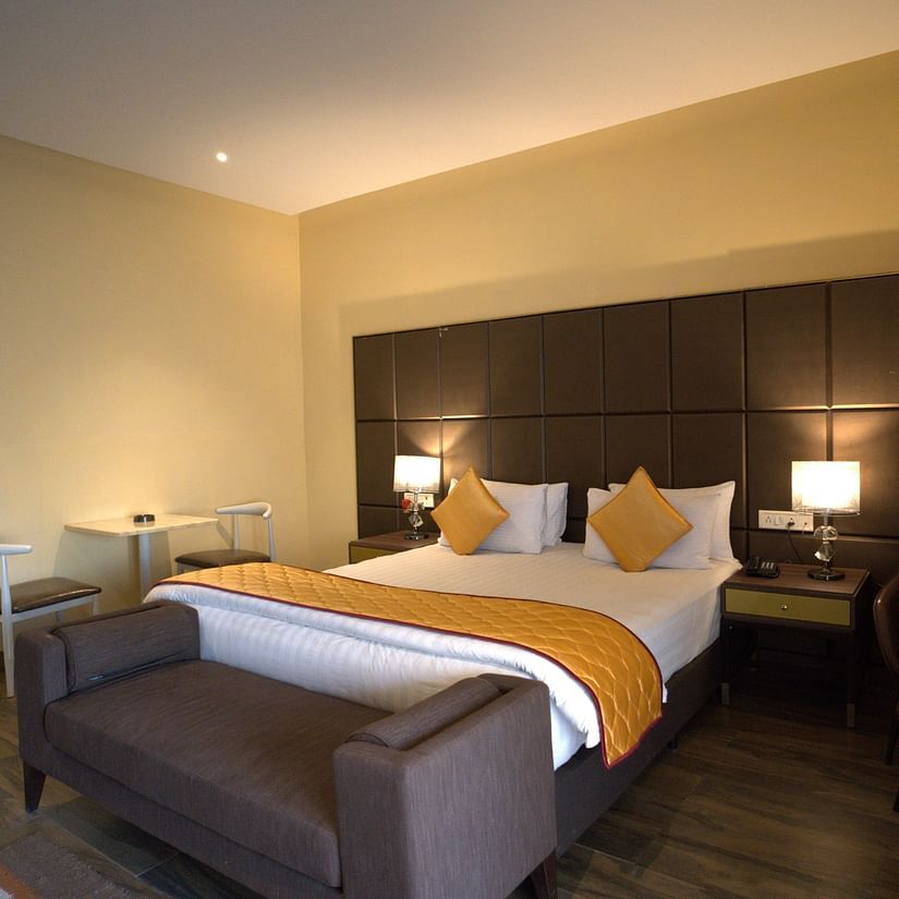 Junior Suite With Jacuzzi at Citrus Classic Resorts and Spa Mahabalipuram ECR featuring a plush bed with a divan at its foot and a couch on one side and a tiny sitting space for two on the other side of the room