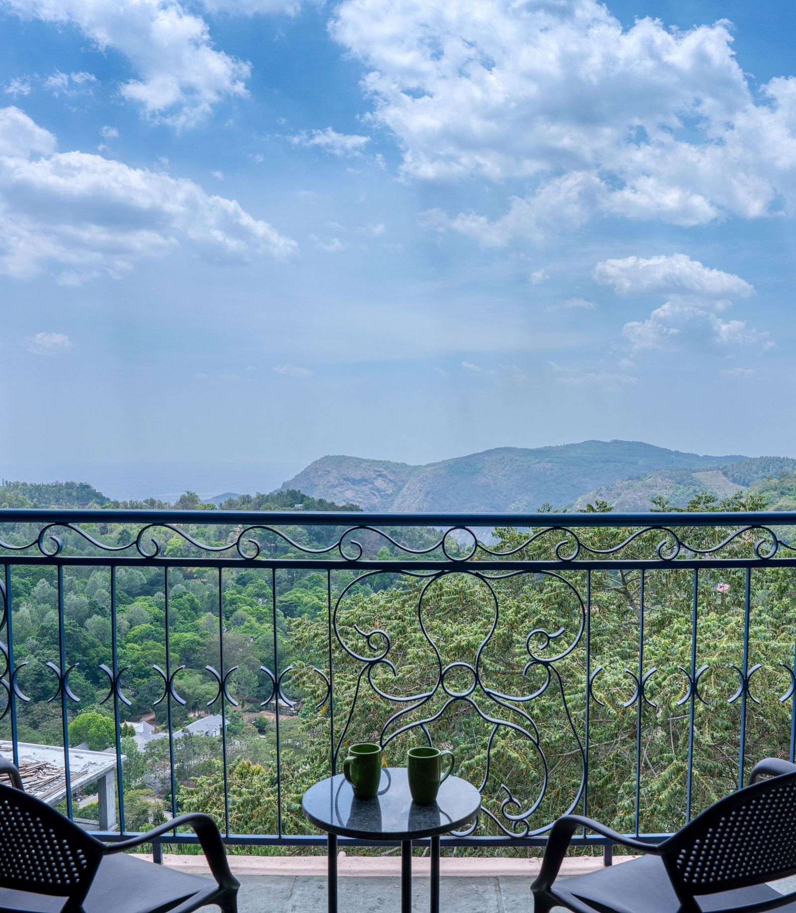 Scenic view from a balcony with two chairs and a table overlooking lush green hills and a clear blue sky | Mango Hill, Yercaud