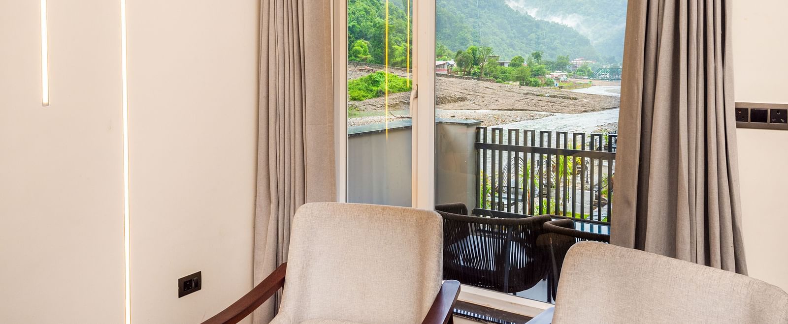 Interior area of Luxury Cottage at DLS Divine Resort and Spa featuring chairs table and river and lush green garden views.