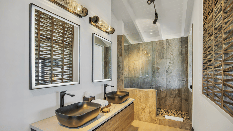 A bathroom at Tamarind Hills Resort and Villas, Antigua, featuring dual black vessel sinks, wood cabinetry, large mirrors, and a sleek walk-in stone shower.