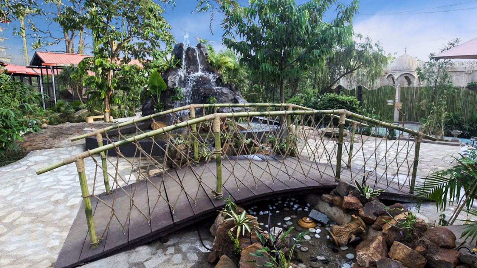 Arched wooden bridge over a small pond with rocks and plants, surrounded by greenery.