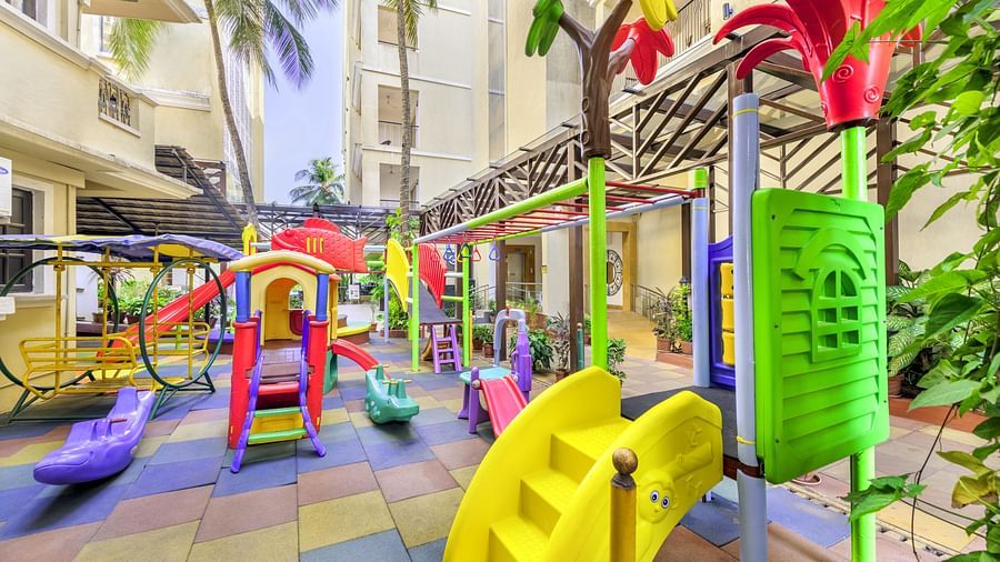 an Outdoor kid's play area with colourful slides, climbers, and swings surrounded by buildings and palm trees - Golden Tulip, Candolim, Goa