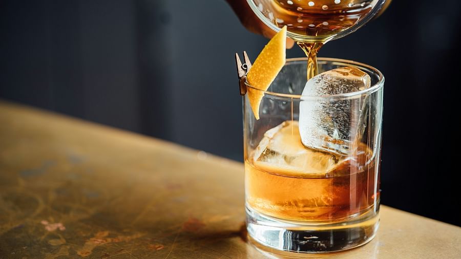 A cocktail being poured onto ice spheres in a glass placed on a bar counter