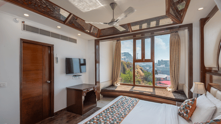 Spacious bedroom with double bed, writing desk, and wide window views at The Solitaire Resort, designed with wooden interiors and cosy ambience for relaxation.