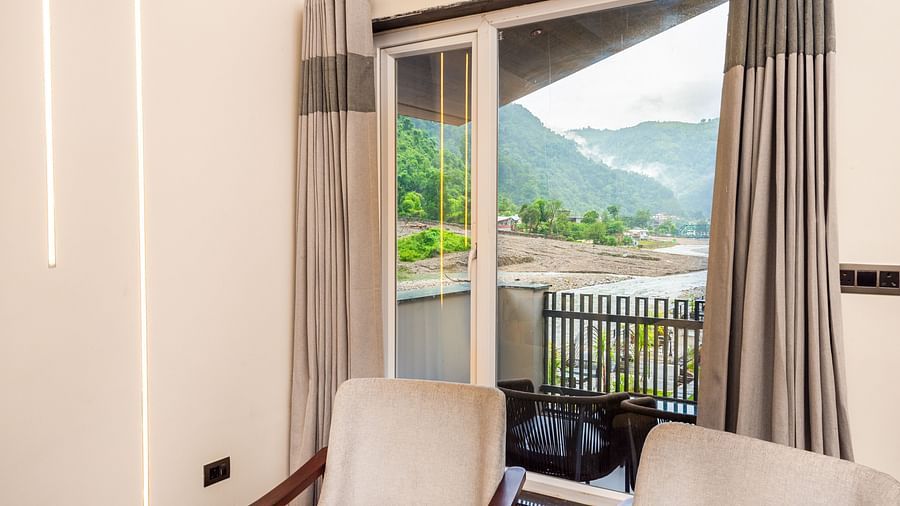 Interior area of Luxury Cottage at DLS Divine Resort and Spa featuring chairs table and river and lush green garden views.