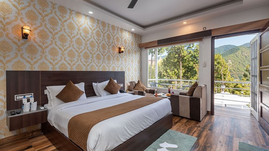  Modern hotel room with a large bed, elegant wallpaper, and wooden flooring; features a seating area, ceiling fan, and a balcony with a scenic mountain view - DLS Nature Trinket Resort, Dalhousie.