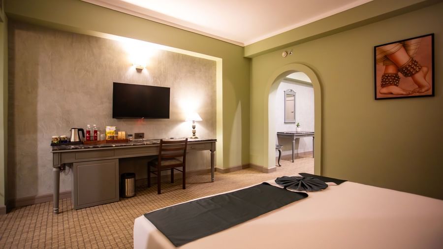 A guest room at Shilton International, Kochi, with a large bed, desk, television, and an archway leading to another area.