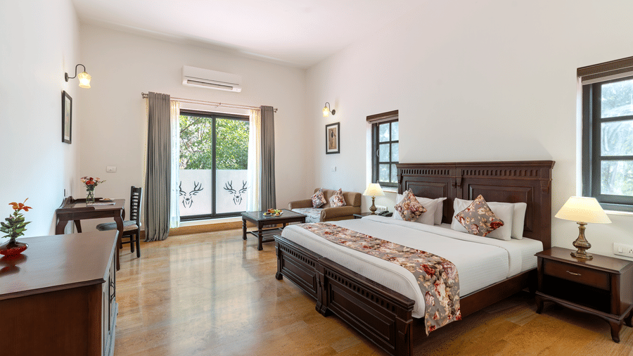 A wide-angle shot of the Superior Room at The Hunting Lodge, Udaipur, showcasing a plush double bed with a floral bed runner spread over it, and french windows at the far end of the room.