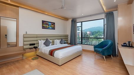 A room with a bed, bed side tables, a chair, and an expansive glass window overlooking the city view - DLS Hotel  Arihant, Haridwar