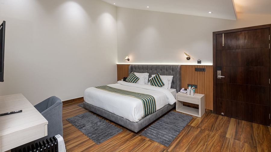 The deluxe room with a bed, bed side table, a chair, a work desk, and warm lighting - DLS The Emerald, Nainital
