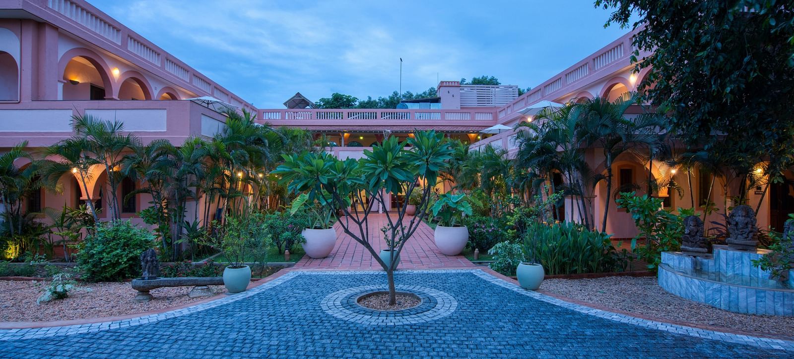 Pathway of a resort with a tree in the middle of it and a backdrop of sky with clouds.