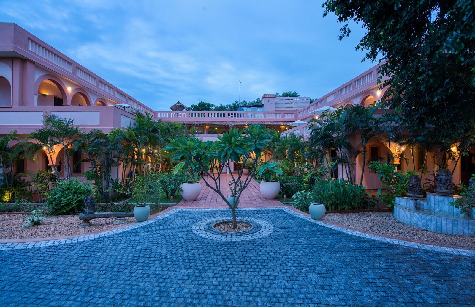 Pathway of a resort with a tree in the middle of it and a backdrop of sky with clouds.