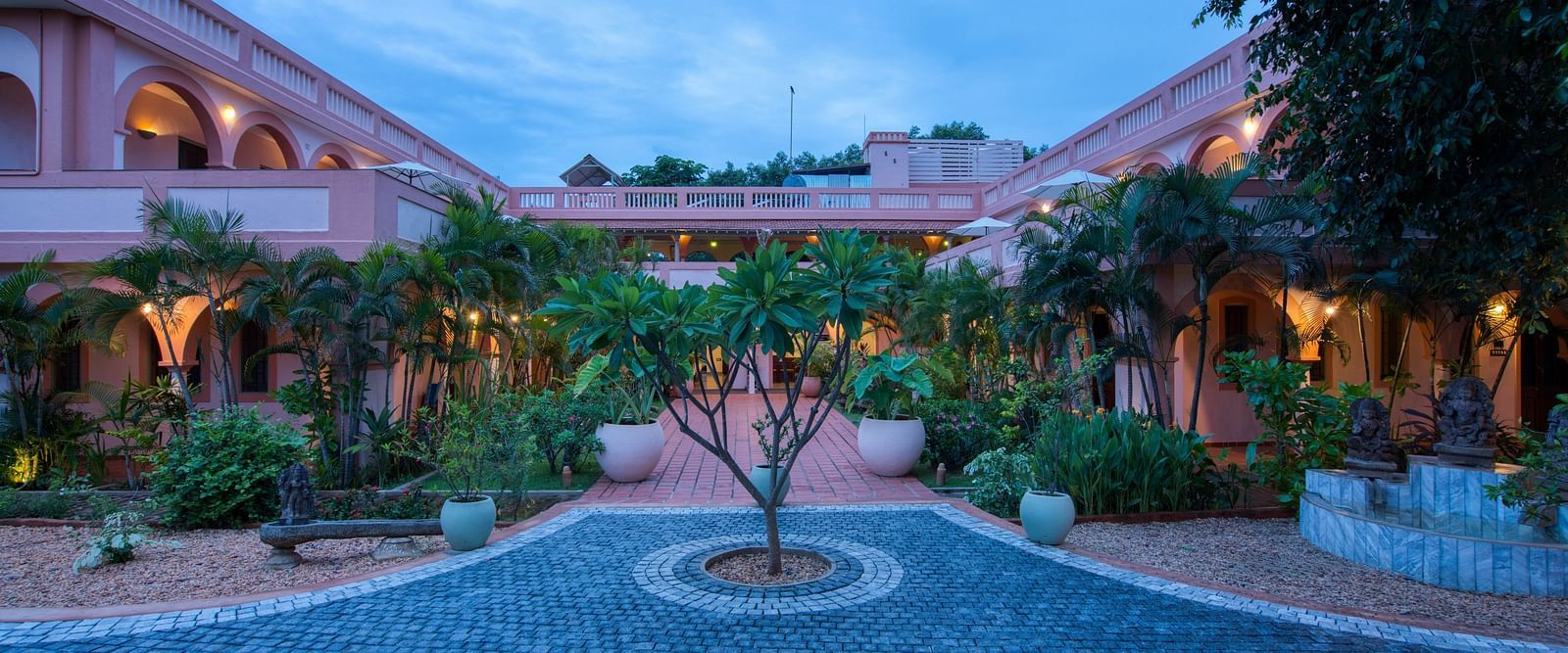 Pathway of a resort with a tree in the middle of it and a backdrop of sky with clouds.