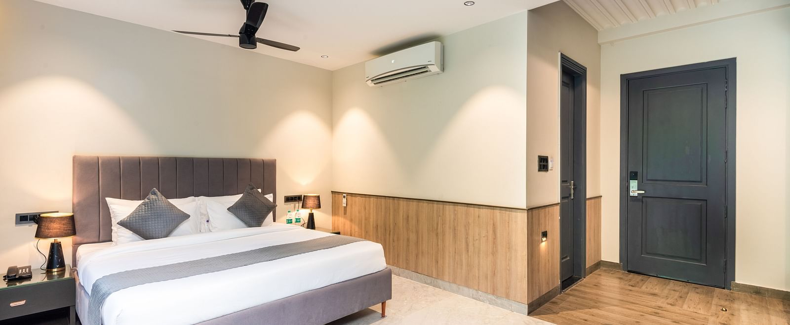 Deluxe Room at DLS Divine River Resort and  Spa featuring a  king bed , side table, warm lighting and a bathroom door.