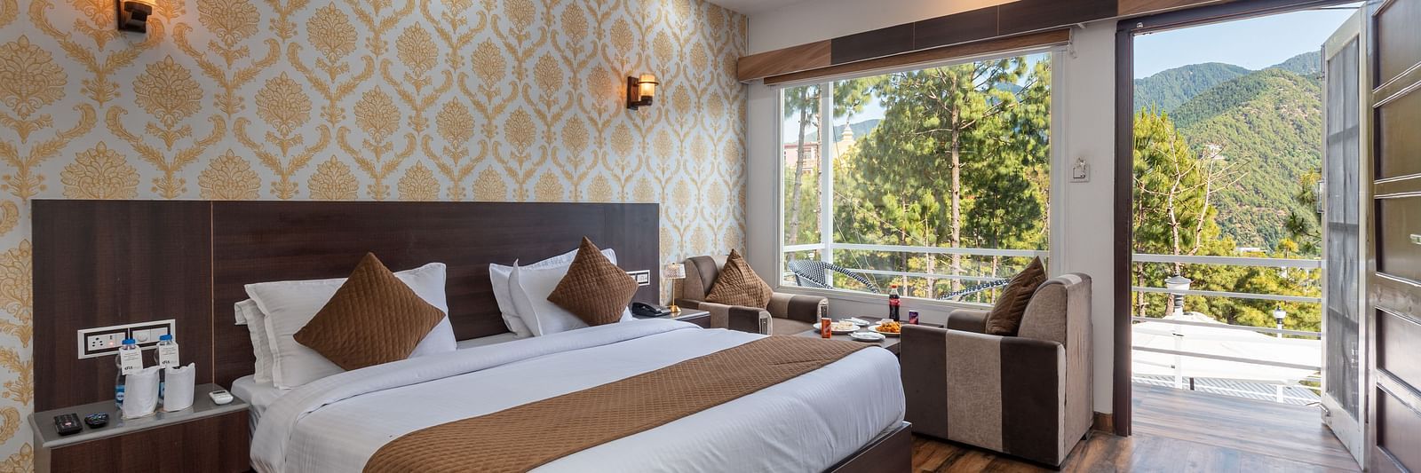  Modern hotel room with a large bed, elegant wallpaper, and wooden flooring; features a seating area, ceiling fan, and a balcony with a scenic mountain view - DLS Nature Trinket Resort, Dalhousie.