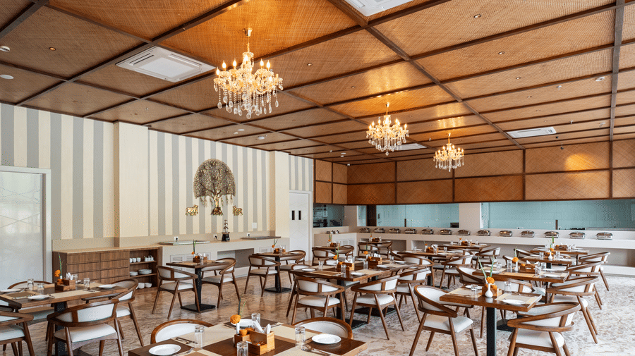 A large restaurant at Osian Valley Resort & Spa featuring a grid of wooden tables and chairs with white cushions. 