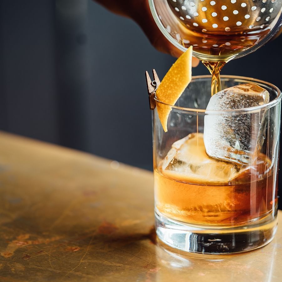 a person pouring a drink on a glass with an ice cube that is placed on a desk