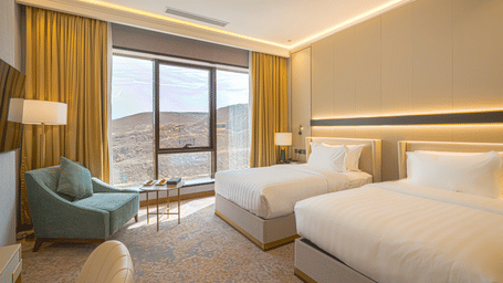 Drawn curtains in a Deluxe Twin Room at Grand Iva Hotel, Abha, showcasing views of the surrounding hills.