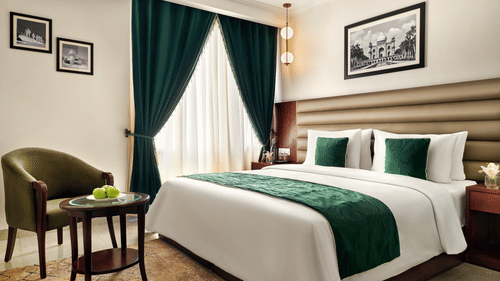 An image of our executive room in new delhi with a large bed placed in front of a green chair - Deventure Sarovar Portico, Patel Nagar
