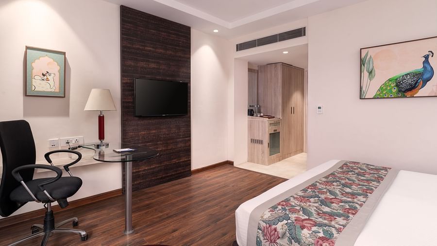 A hotel bedroom with a bed, a seating area, and a TV.