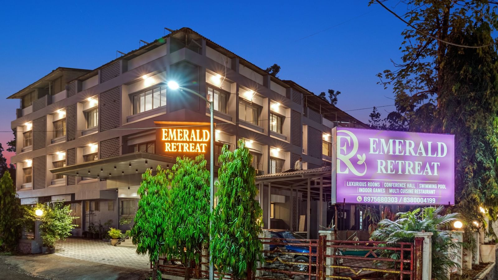 Well-lit entrance of Emerald Retreat, Tungarli with signage, landscaped greenery, and parked cars.