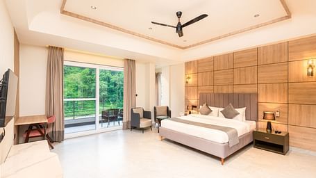 Overview of Premium Room at DLS Divine River Resort and  Spa featuring a  king bed , side table, warm lighting, chair and balcony with forest views.