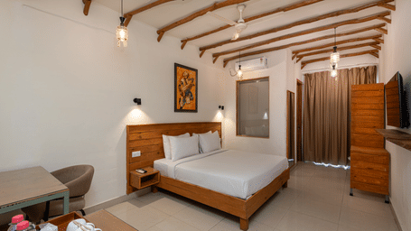 Spacious room with a king size bed, pendant lights, wooden furniture, curtains, and seating area at Ekawa Ganga, Rishikesh.