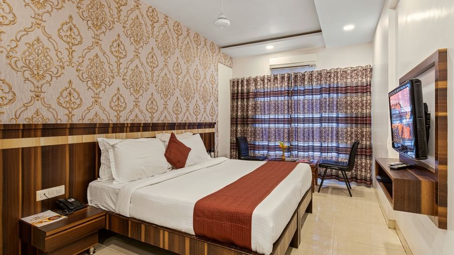 King size bed room at Mayur Retreat with beige wallpaper, wooden wall panelling, and large curtained window
