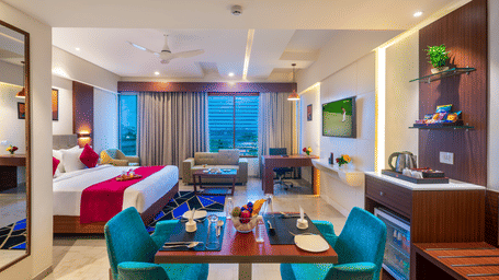 A spacious bedroom in Lords Eco Inn Shapar Rajkot, featuring a double bed, mini bar, lounge chair, in-room dining area, and modern interiors 