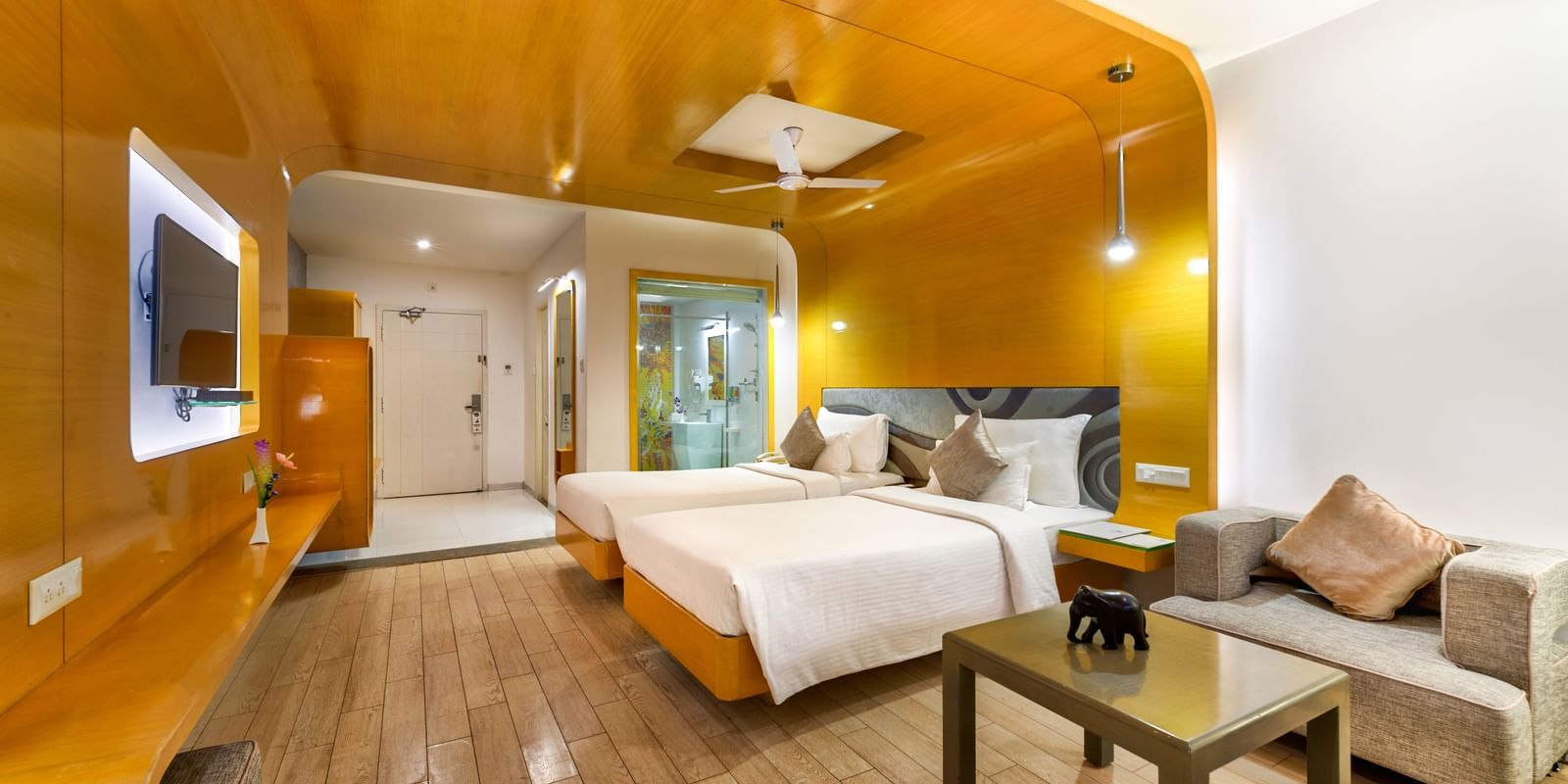A room with twin beds, golden wall panel and wooden furniture featuring a seating space at Grande Bay Resort & Spa.