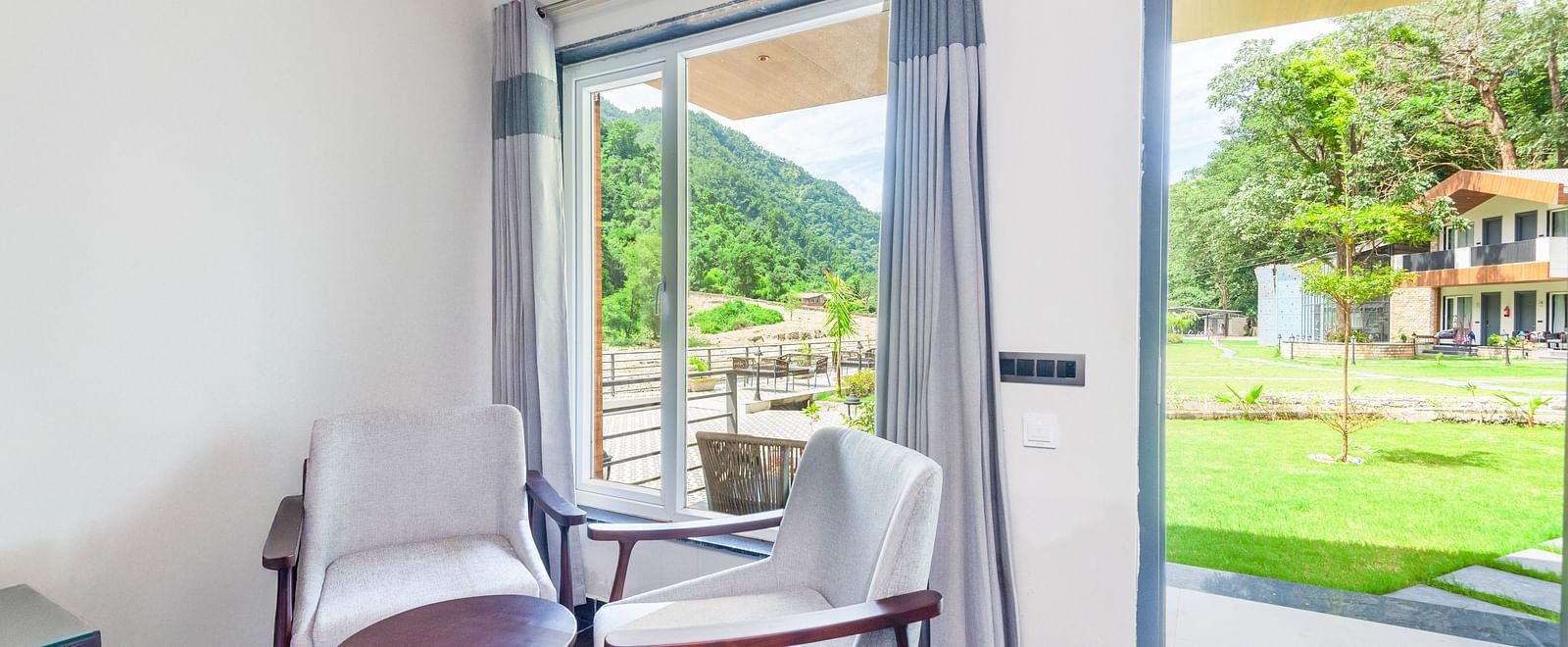 Interior area of Luxury Cottage at DLS Divine Resort and Spa featuring chairs table and lush green garden views.