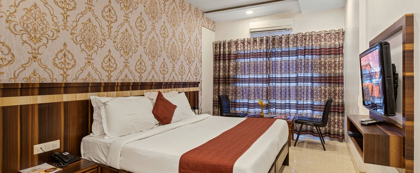King size bed room at Mayur Retreat with beige wallpaper, wooden wall panelling, and large curtained window