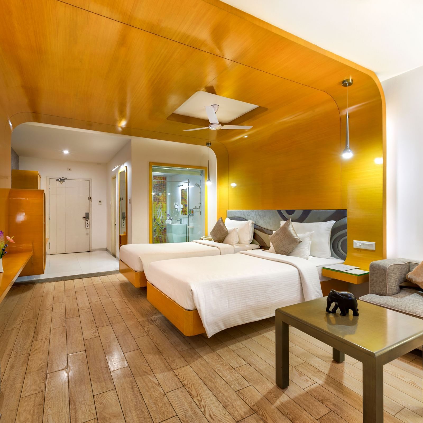 A room with twin beds, golden wall panel and wooden furniture featuring a seating space at Grande Bay Resort & Spa.