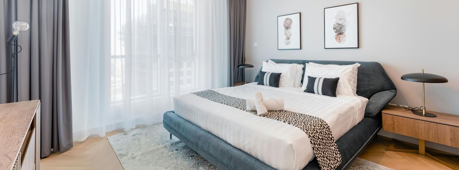 A room featuring a large bed, chandelier, spacious window, and stylish furnishings