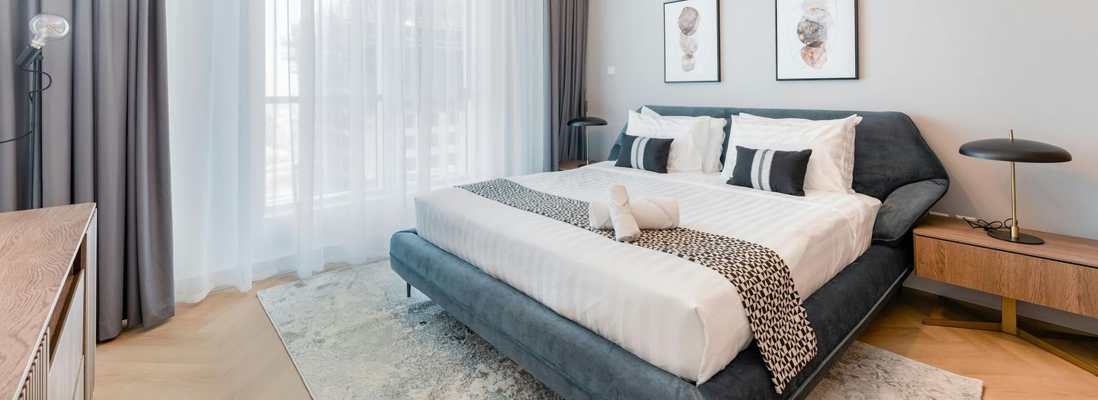 A room featuring a large bed, chandelier, spacious window, and stylish furnishings
