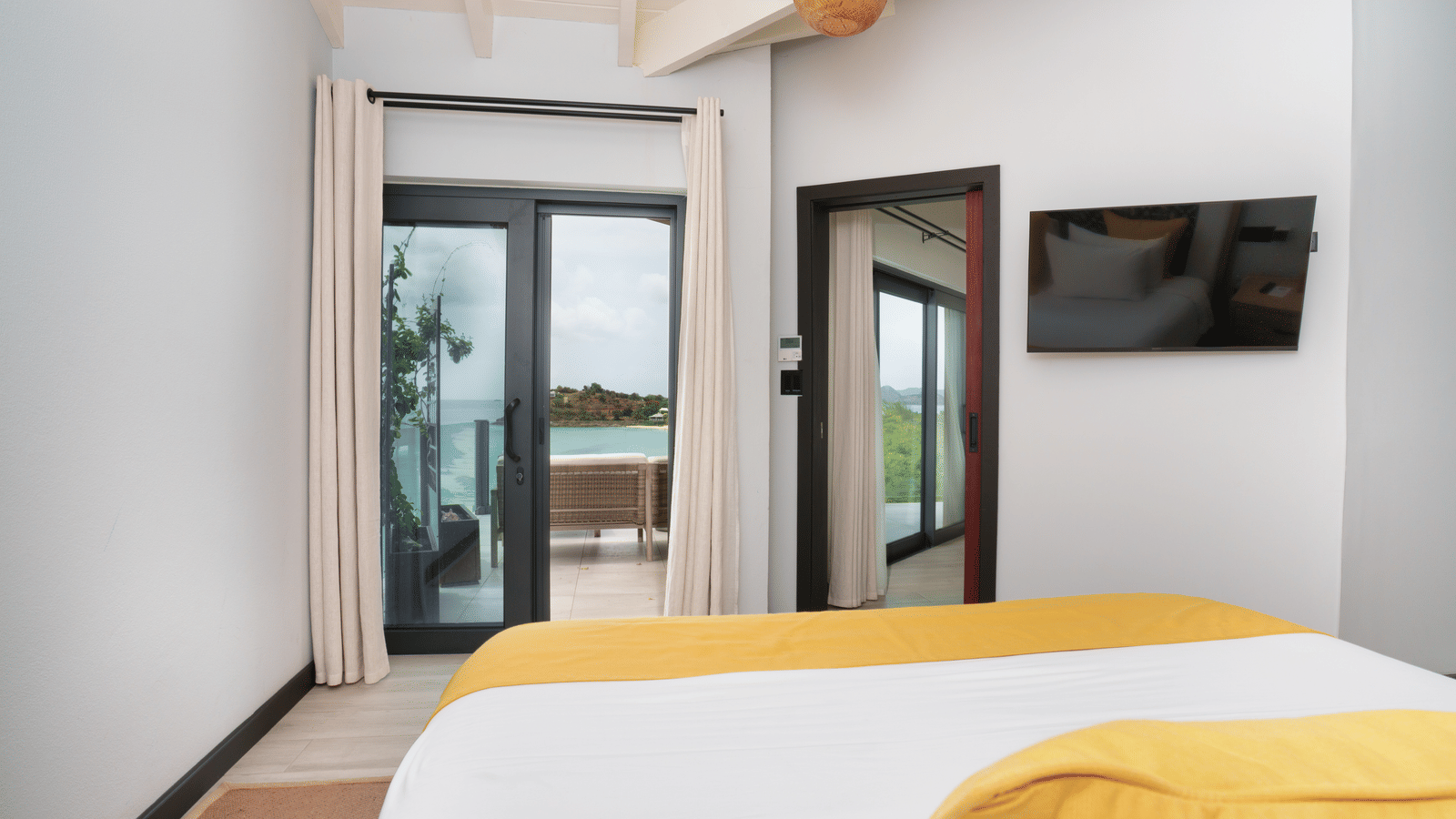 Bedroom with a large bed, wall-mounted television, bedside tables, and glass doors opening to the terrace at Ocean 19, Tamarind Hills Resort and Villas.