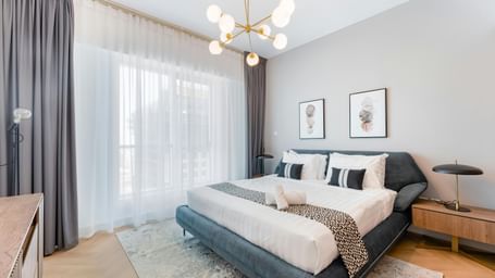 A room featuring a large bed, chandelier, spacious window, and stylish furnishings