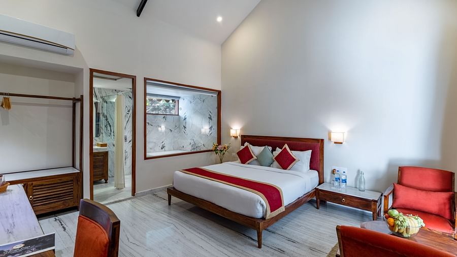 full view image of the luxury bathtub villas featuring a king size bed in the centre of the room and a family seating area with red cushioned chairs at aranya vilas in udaipur